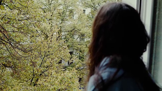 德国柏林，一个美丽的年轻女子从旧公寓大楼望向窗外的街道。视频素材