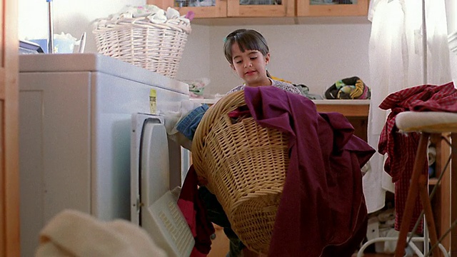 中等身材的女孩把衣服从烘干机里拿出来，堆在篮子里，然后拿起篮子视频下载
