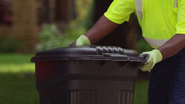 垃圾收集工人把一桶垃圾倒进垃圾车里。视频素材