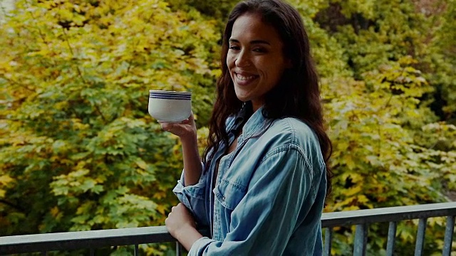 在德国柏林的一个典型的老公寓大楼里，一个年轻漂亮的女人在阳台上喝着咖啡看着院子。视频素材