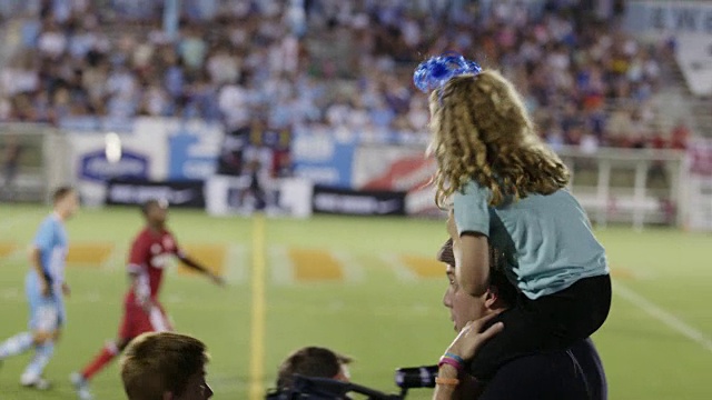 在一场职业足球比赛中，加油的体育迷和肩上的小女孩与朋友击掌。视频下载