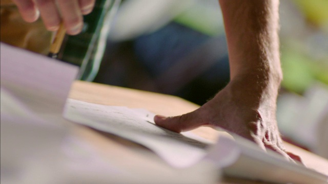 一个富有创造力的年轻人用铅笔敲击桌子，在坐标纸上做笔记视频素材