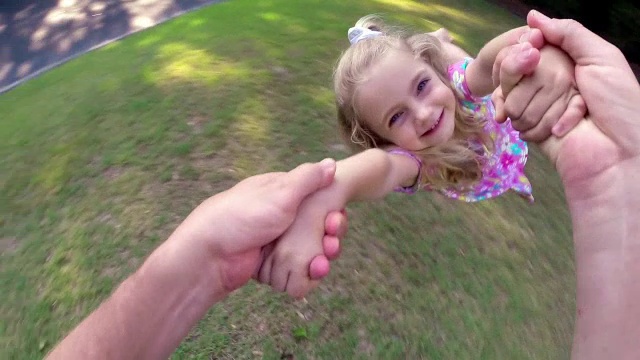可爱的小女孩在父亲的怀抱里在前院旋转视频素材