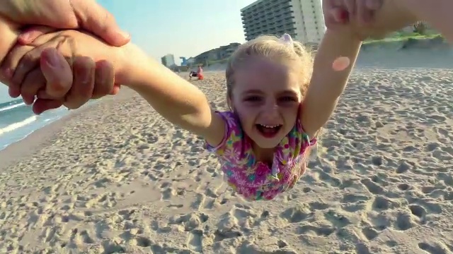 在阳光明媚的海滩上，可爱的小女孩在爸爸的怀里旋转视频素材