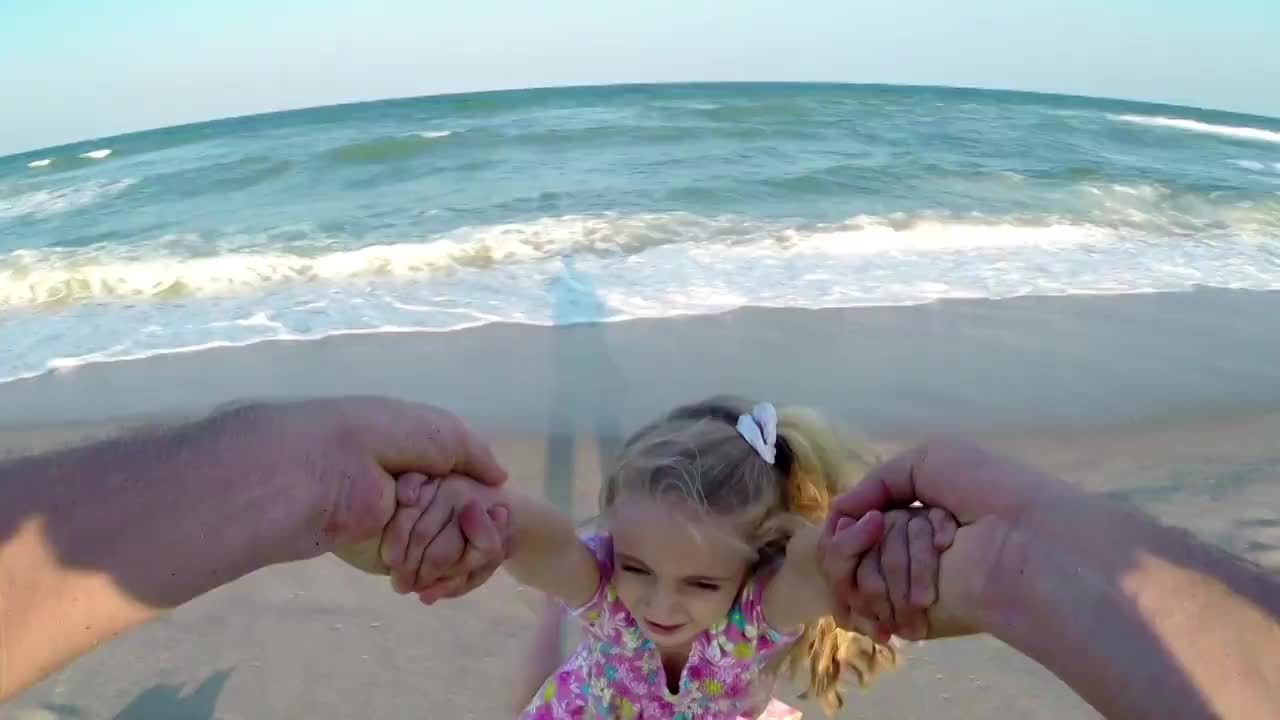 当海浪在阳光明媚的海滩上拍打时，父亲带着女儿四处摇摆视频下载