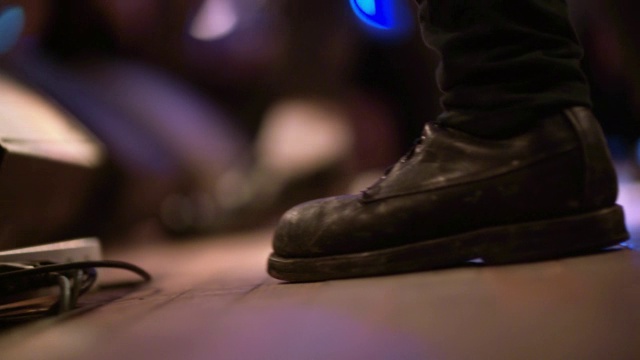 在拥挤的摇滚音乐会上，吉他手在舞台上有节奏地敲靴子视频素材