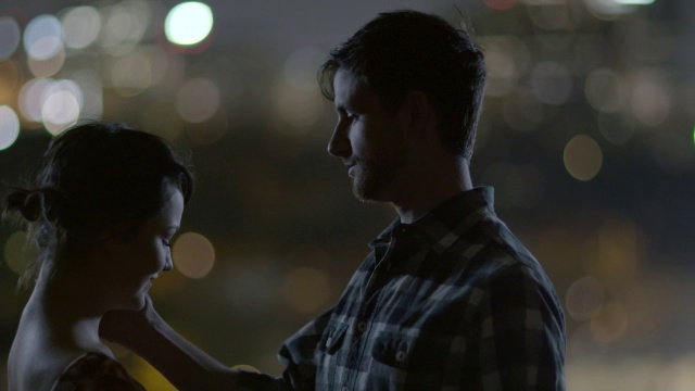 在城市的灯光下，一对年轻的情侣深情地凝视着对方的眼睛，手牵着手视频素材