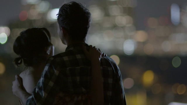 一个年轻人把他的女朋友拉到他身边，他们一起看着夜晚的城市天际线视频素材
