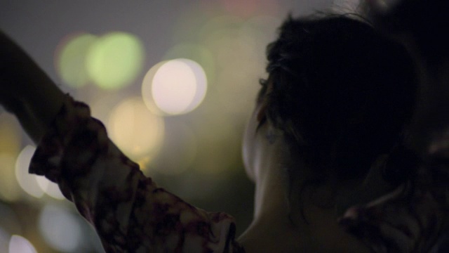 在城市的灯光下，年轻的女子在空中挥舞着她的手，亲吻着她的男朋友视频素材