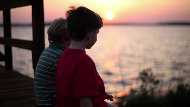 两个男孩边聊天边看五彩缤纷的天空和波浪形的海洋。视频素材