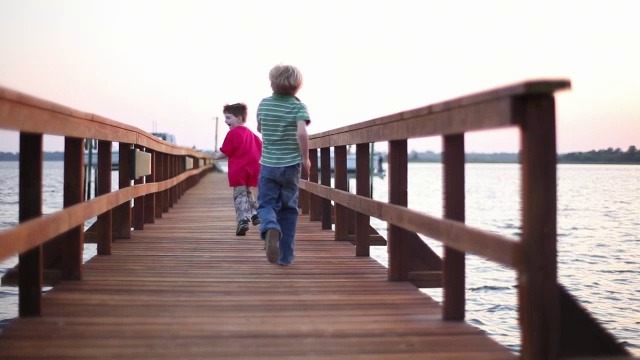两个男孩嬉闹着跑下一个海洋码头。视频素材