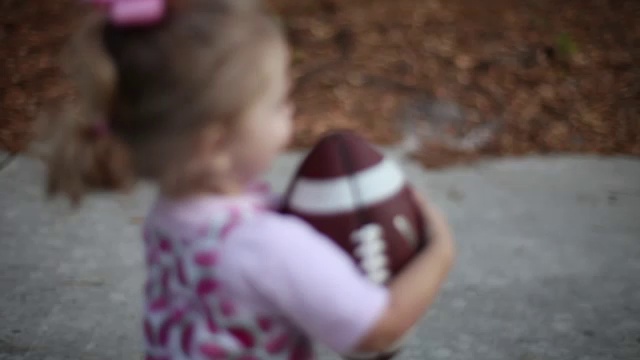 一个蹒跚学步的小女孩拿着足球在院子里跑来跑去。视频素材