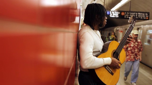 MED侧写黑人靠在红墙弹吉他在地铁站列车离开人们走过视频素材