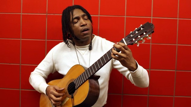 一名黑人靠在地铁站的红墙上，边唱边弹吉他视频素材