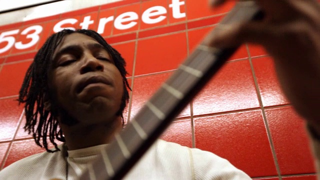 一名黑人靠在地铁站的红墙上弹吉他视频素材