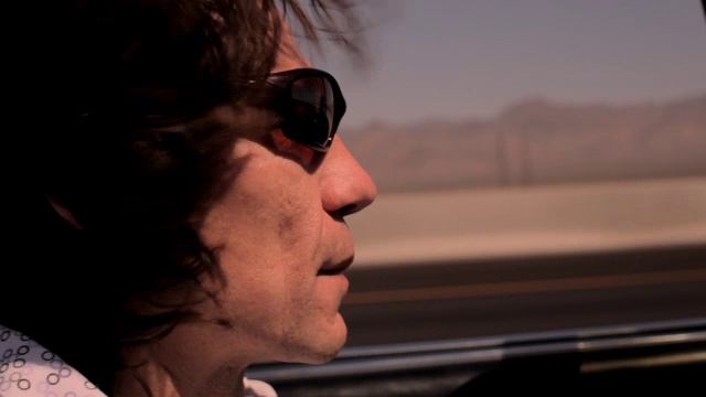 一个男人开着一辆老式敞篷车沿着一条风景优美的沙漠公路行驶。视频下载