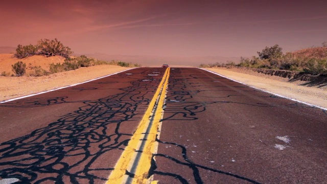 一辆红色的老式敞篷车驶过沙漠公路上修补过的裂缝。视频下载