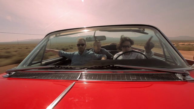 三个男人开着一辆红色复古敞篷车在沙漠公路上兜风。视频下载