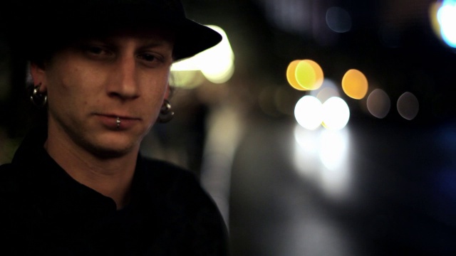 一个年轻人在城市的街道上点燃了一根香烟，然后转过头看着镜头。视频下载