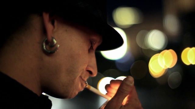 一个年轻人在城市的街道上点燃了一根香烟，转过身看着镜头。视频下载