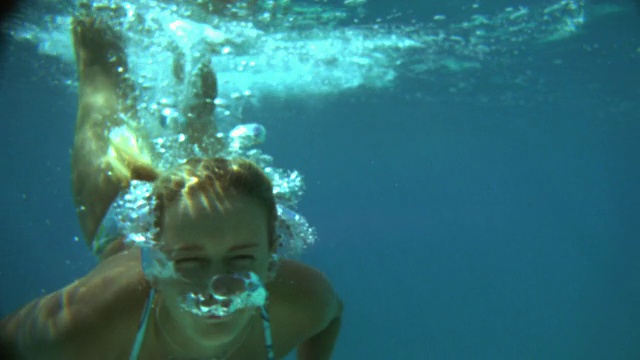 慢动作近景女子跳水到水下的冲浪板上/气泡从鼻子视频素材