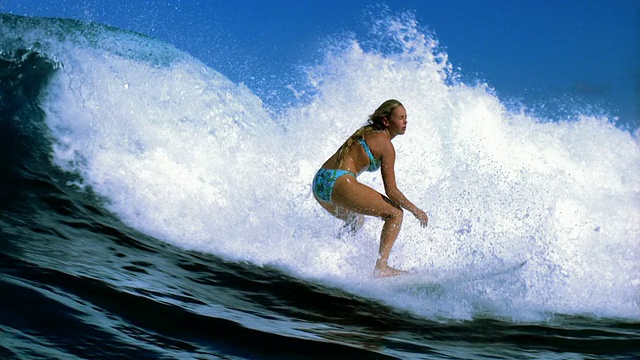 慢动作宽镜头跟踪拍摄女性冲浪者划桨，站在冲浪板上/骑浪视频素材