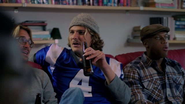 一群年轻的成年男性喝着啤酒在电视上观看体育节目视频素材