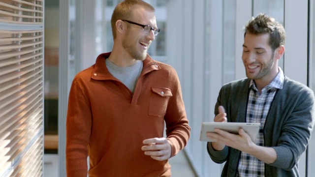 男女商业伙伴在白板上写字，两位时髦的商人一边走在办公室走廊上，一边用平板电脑讨论战略(摄影)视频下载