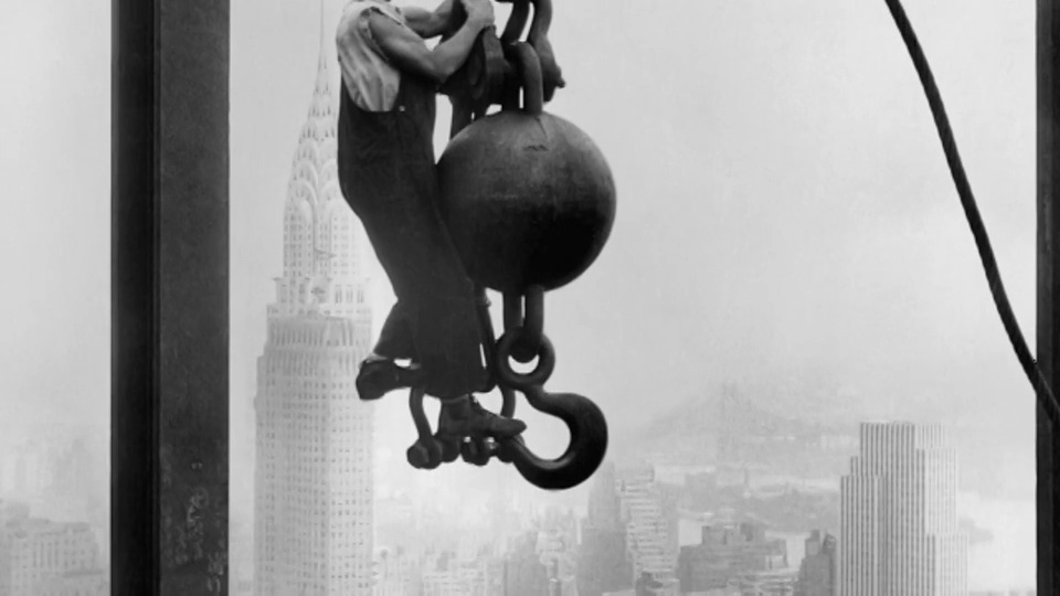 在帝国大厦的建筑工地上，一名钢铁工人吊在曼哈顿街道上方的吊钩上。视频下载