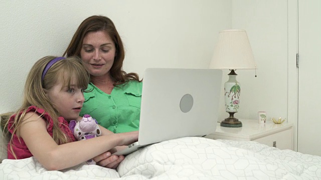 母亲和她的女儿坐在床上，使用笔记本电脑视频素材