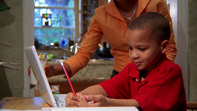中等镜头的年轻黑人男孩在电脑前工作/黑人妇女从厨房走出来帮助他视频下载