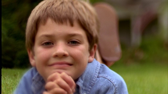 一个小男孩微笑着在绿色的草地上休息。视频素材