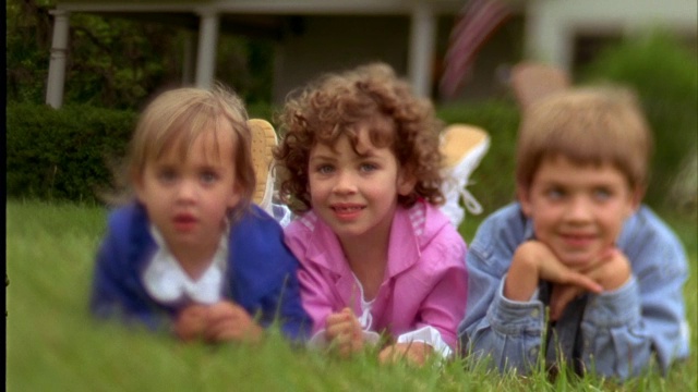 一个男孩和两个女孩微笑着在绿色的草地上放松。视频素材