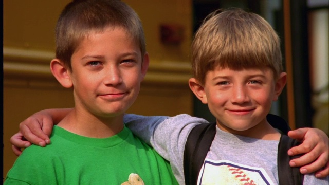 两兄弟站在一起，微笑着站在他们的校车前。视频下载