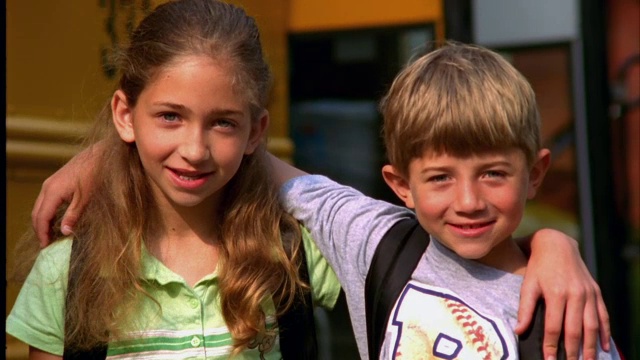 一对兄妹站在他们的校车前微笑着。视频下载