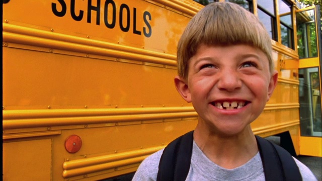 一个小男孩在校车前面笑着。视频素材