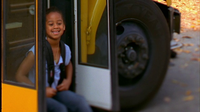 一个小女孩在校车的楼梯上微笑着。视频素材