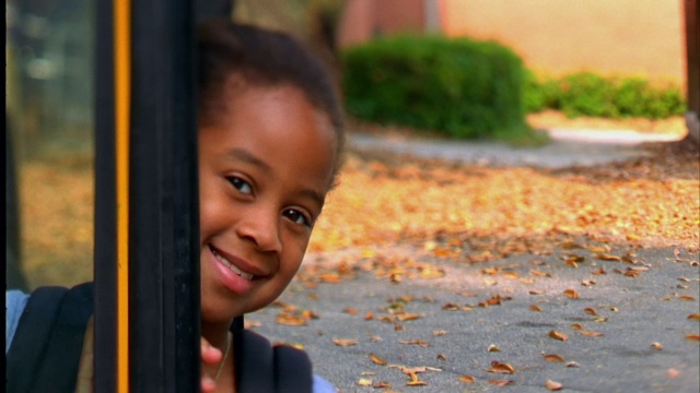 一个小女孩微笑着，从她的校车的门口偷看。视频素材