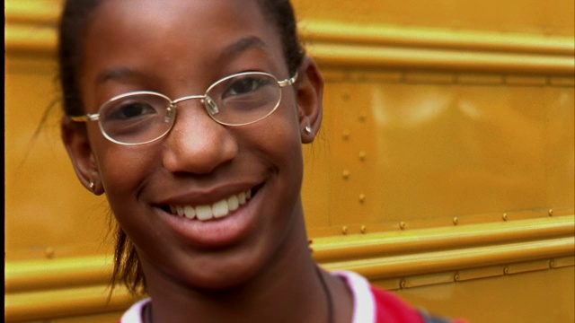 一个女孩在校车前微笑着。视频素材
