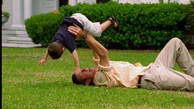 一个男人顽皮地把躺在草地上的儿子举过头顶。视频素材