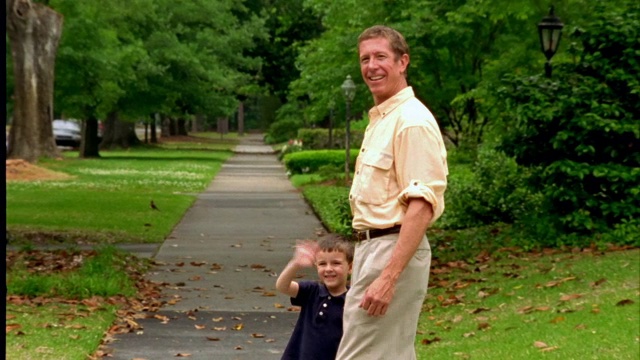 一个小男孩和他爸爸站在人行道上。视频素材