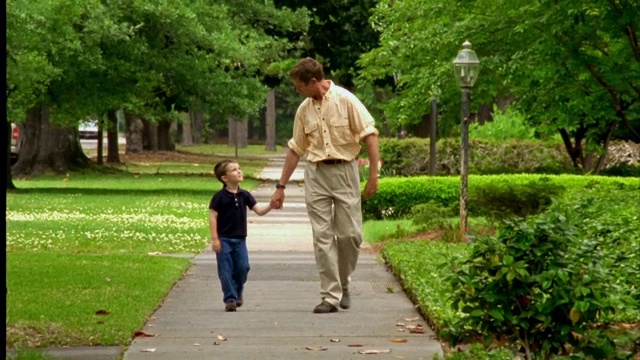一对父子手牵着手走在人行道上。视频素材
