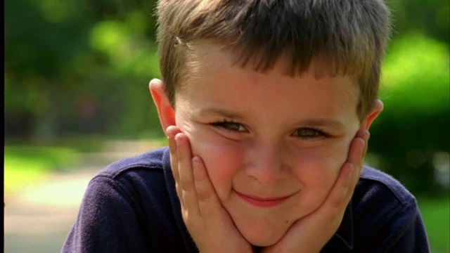 一个小男孩双手捂着脸微笑着。视频素材