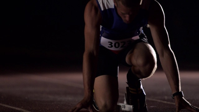 一名运动员蹲在跑道上的起跑点前，开始跑步和练习跳跃。视频素材
