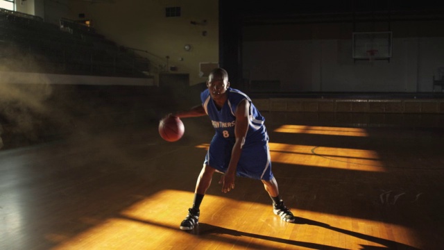 一个篮球运动员在空旷的看台前练习他的控球技巧。视频下载