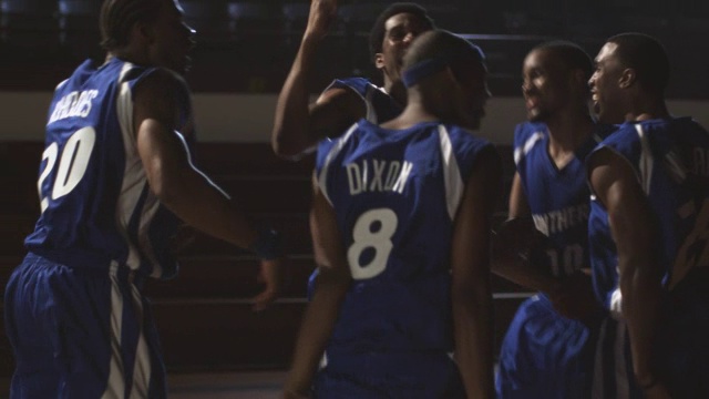 在一个看台空无一人的篮球馆里，一支蓝队在一支红队附近庆祝一场篮球比赛。视频素材
