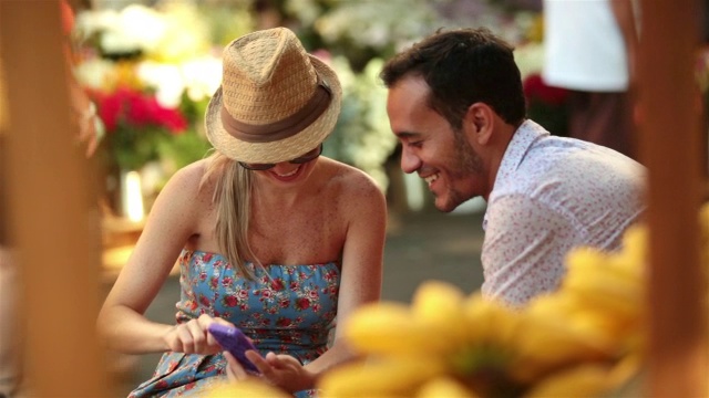 在繁忙的巴西市场，一对可爱的情侣一边看智能手机一边聊天视频素材