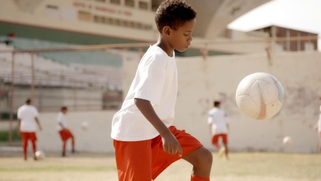 一个巴西男孩在干球场上的青年联赛练习中举起并踢足球视频素材