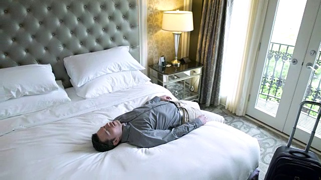 一个年轻人走进酒店房间，倒在了床上视频素材