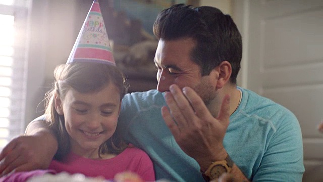 在家庭聚会上，小女孩用生日蛋糕糖霜戳爸爸的鼻子。视频购买